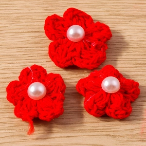 Vue détaillée de trois fleurs rouges au crochet avec perles centrales sur fond en bois