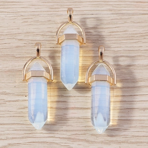 Detailed view of three hexagonal opalite bullet pendants with gold metal bails on wood