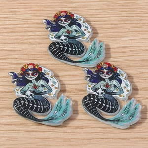 Three acrylic skull mermaid charms with Day of the Dead flower crowns on wood background