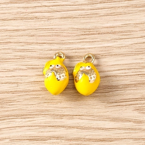 Close-up of two yellow lemon vegetable pendants with gold rings on wood surface