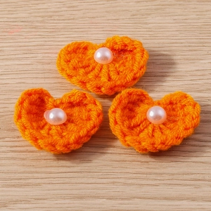 Détail de trois cœurs en crochet orange faits main avec perles sur fond en bois