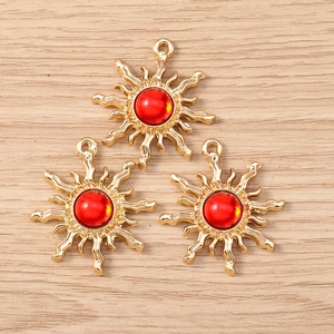 Three gold sun pendants with red gemstones for DIY jewelry making on wood surface