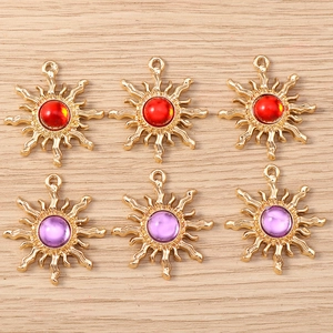 Detail view of gold sun-shaped pendants with red and purple faux gemstones on wood