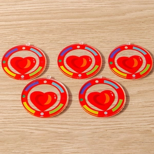 Flat lay of five round acrylic rainbow pendants with red heart motif on wooden surface