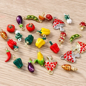Assorted enamel vegetable pendants including corn and pepper on a wooden surface