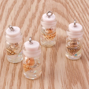 Close-up of glass bottle charms with shells and glitters on a light wooden background