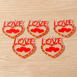 Macro detail of red acrylic heart charms with LOVE text and floral patterns on wood