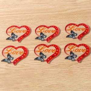 Detailed view of six acrylic heart charms with Love text and butterfly on wood