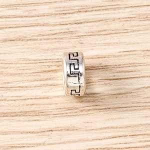 Vue détaillée d'une perle en argent cylindrique avec motif grec sur fond de bois