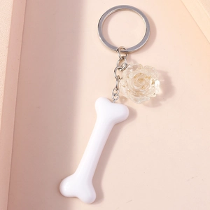 Close-up of white bone resin keychain with a gold foil rose floral charm on pink surface