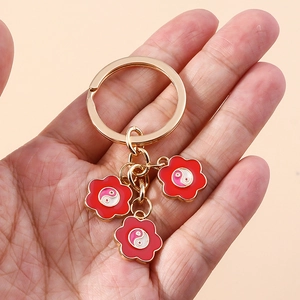 Dettaglio di un portachiavi dorato con tre ciondoli a fiore rosso e motivi Yin Yang Taiji