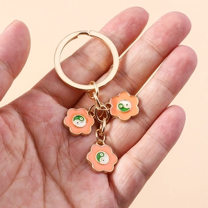 Dettaglio del portachiavi dorato con fiori arancioni e simboli Tai Chi cinesi