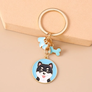 Makroansicht goldener Schlüsselanhänger mit Emaille-Shiba Inu und blauem Knochen-Anhänger