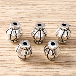 Five vintage silver lantern shaped spacer beads on light wood for DIY jewelry crafting