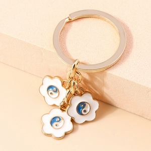 Dettaglio portachiavi dorato con tre ciondoli a fiore bianco e simboli tai chi blu e bianchi