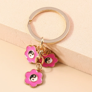 Dettaglio portachiavi dorato con tre fiori in smalto rosa e simboli Tai Chi Taiji