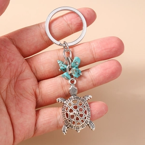 Silver hollow turtle keychain with turquoise stones held in hand on orange background