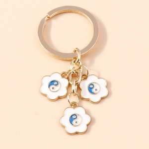 Portachiavi dorato con tre ciondoli a forma di fiore bianco e motivi Tai Chi blu e bianchi