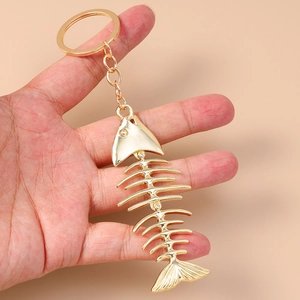 Creative gold fish bone keychain with alloy keyring held against pink background