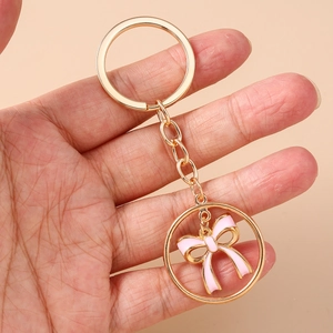Elegant gold keychain featuring a pink enamel bow charm held in hand for scale