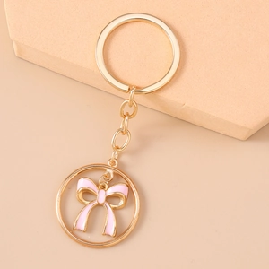 Close-up of golden keychain with pink enamel bow charm in elegant warm background