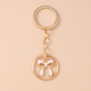 Close-up of golden alloy keychain featuring a delicate pink enamel bow charm in a round frame