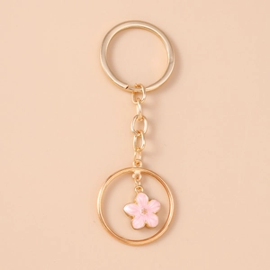 Detail of a golden keychain featuring a pink enamel flower charm and round pendant