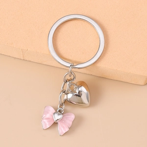 Close-up of silver heart and pink bow charms on a metal keychain for bags
