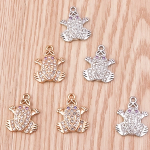 Detailed view of six sparkling frog pendants in gold and silver with purple rhinestone eyes