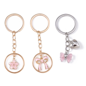 Detail of flower and bowknot metal keychains with pink enamel charms on white background