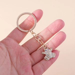 Close-up of golden frog keychain with sparkling rhinestones on light pink background