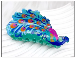 Détail macro d'une grande pince à cheveux paon avec des plumes colorées sur un plateau blanc