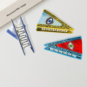 Three triangular PVC hair claws with evil eye design on a textured surface