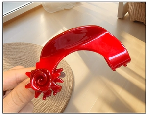 Detailed close-up of a bright red resin hair claw clip with elegant 3D rose flower accents