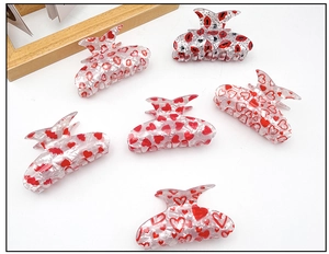 Détail de six pinces à cheveux en acrylique aux motifs de cœurs et lèvres rouges sur marbre