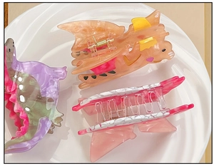 Flat lay of colorful acetate hair claws in cat and dinosaur shapes on a ceramic tray