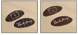 Detailed close-up of brown checkered and solid fabric hair clips with bear embroidery