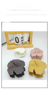 Detail view of four matte flower-shaped hair claws in ivory, pink, grey, and yellow