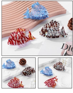 Detailed view of three fish-shaped acetate hair claws in blue, red, and tortoiseshell