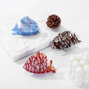 Three goldfish-shaped acetate hair claws in blue, red, and brown on white fabric background