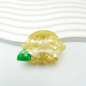 Pince à cheveux citron jaune avec texture perlée et feuille verte sur fond blanc