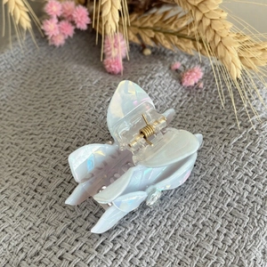 Iridescent white acetate claw clip with pearl-like luster on a textured fabric background