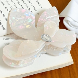 Iridescent white flower hair claw clip with crystal center on a vintage book background