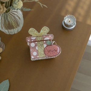 Pink glitter acrylic Christmas gift and apple hair claw clip on a cozy wooden desk