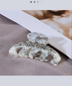 Close-up of pearl luster hair claw clip with rhinestones and marble texture detail