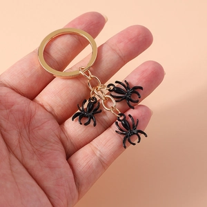 Handheld view of a gold keychain featuring three realistic black spider charms on a ring