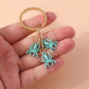 Minimalist gold-plated spider keychain with three mint blue charms held in hand