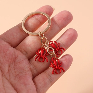 Minimalist red spider keychains with gold metal ring held by hand on beige background