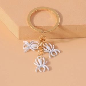 Detailed close-up of three white spider charms hanging from a gold metal keychain ring