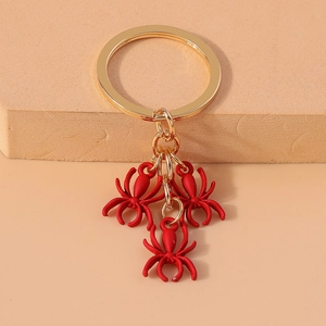 Close-up of golden keychain with three red spider charms on a minimalist display pedestal
